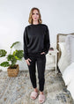 Woman wearing a black lounge  outfit standing in a bedroom.