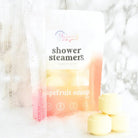 Shower Steamer 6pk Grapefruit Orange packaging with shower steamers in a relaxing setting.