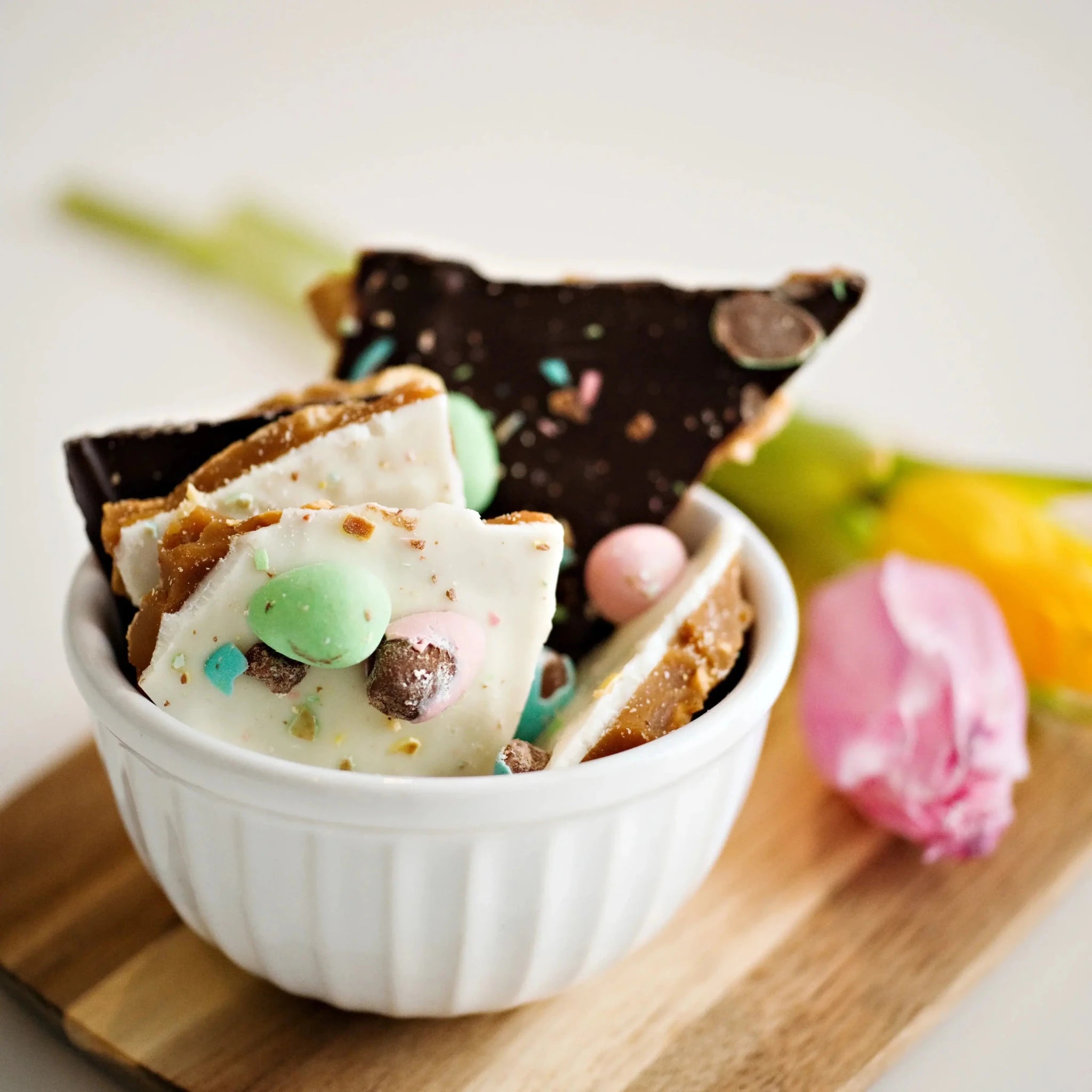 Utoffeea Canada Handcrafted Toffee pieces in a white bowl surrounded by flowers.