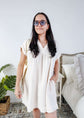 Woman wearing a white dress and sunglasses in a room with a plant and bed. Scarlett Ellie V-Neck Gauze Dress | Lightweight Summer Dress | Cloud Nine Pajamas