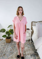 Scarlett Ellie V-Neck Gauze Dress | Lightweight Summer Dress | Cloud Nine Pajamas Woman wearing a pink dress standing in a bedroom with a plant and bed in the background.