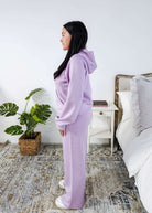 Person wearing a lavender tracksuit standing in a bedroom.