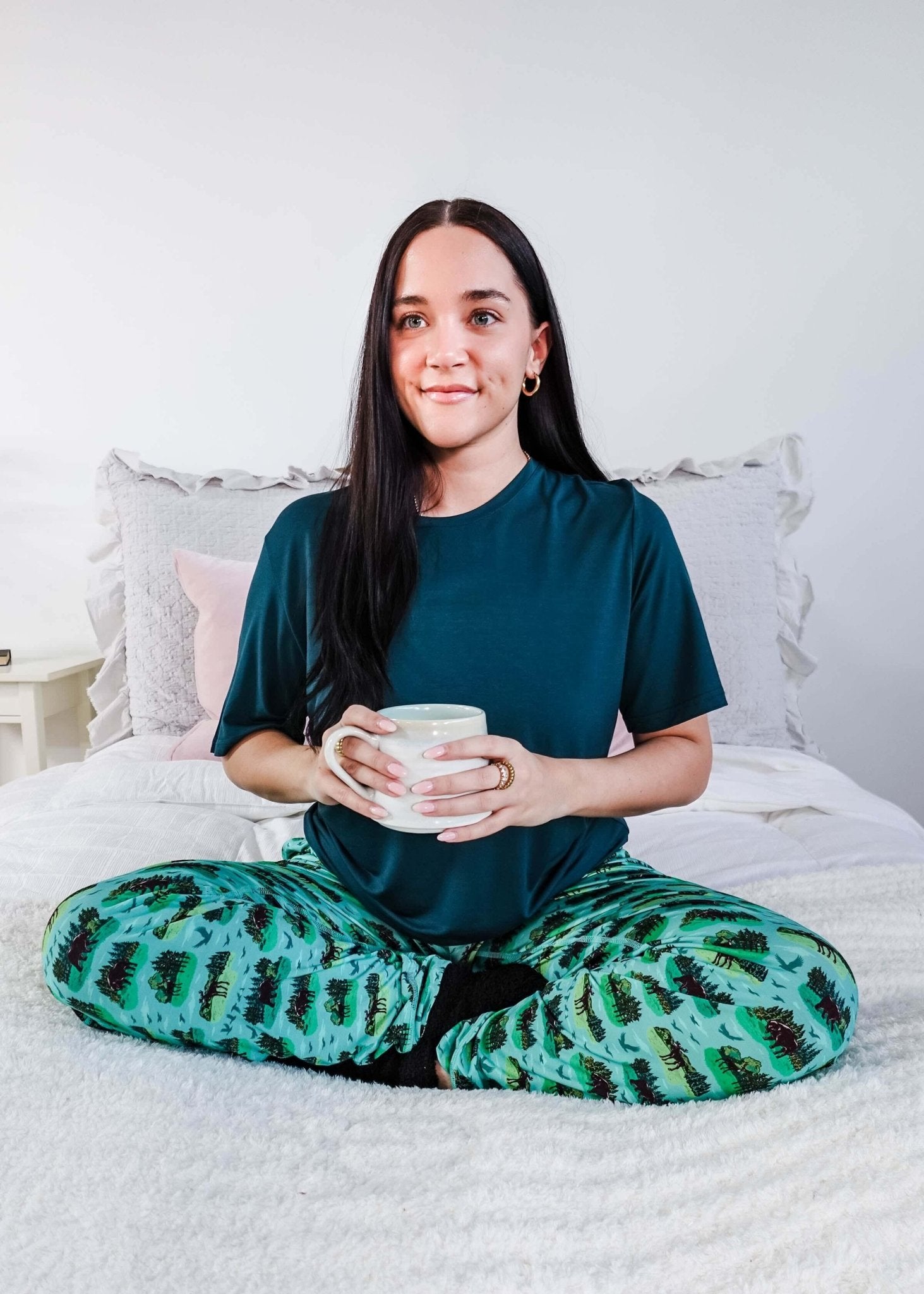 Model wearing Wildlife Aqua Unisex Bamboo Joggers while holding a cup, sitting on a bed.