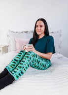 Person wearing Wildlife Aqua Unisex Bamboo Joggers by Bob's Sleepwear Co. while enjoying a drink on a bed.