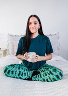 Model wearing Wildlife Aqua Unisex Bamboo Joggers while holding a cup, sitting on a bed.