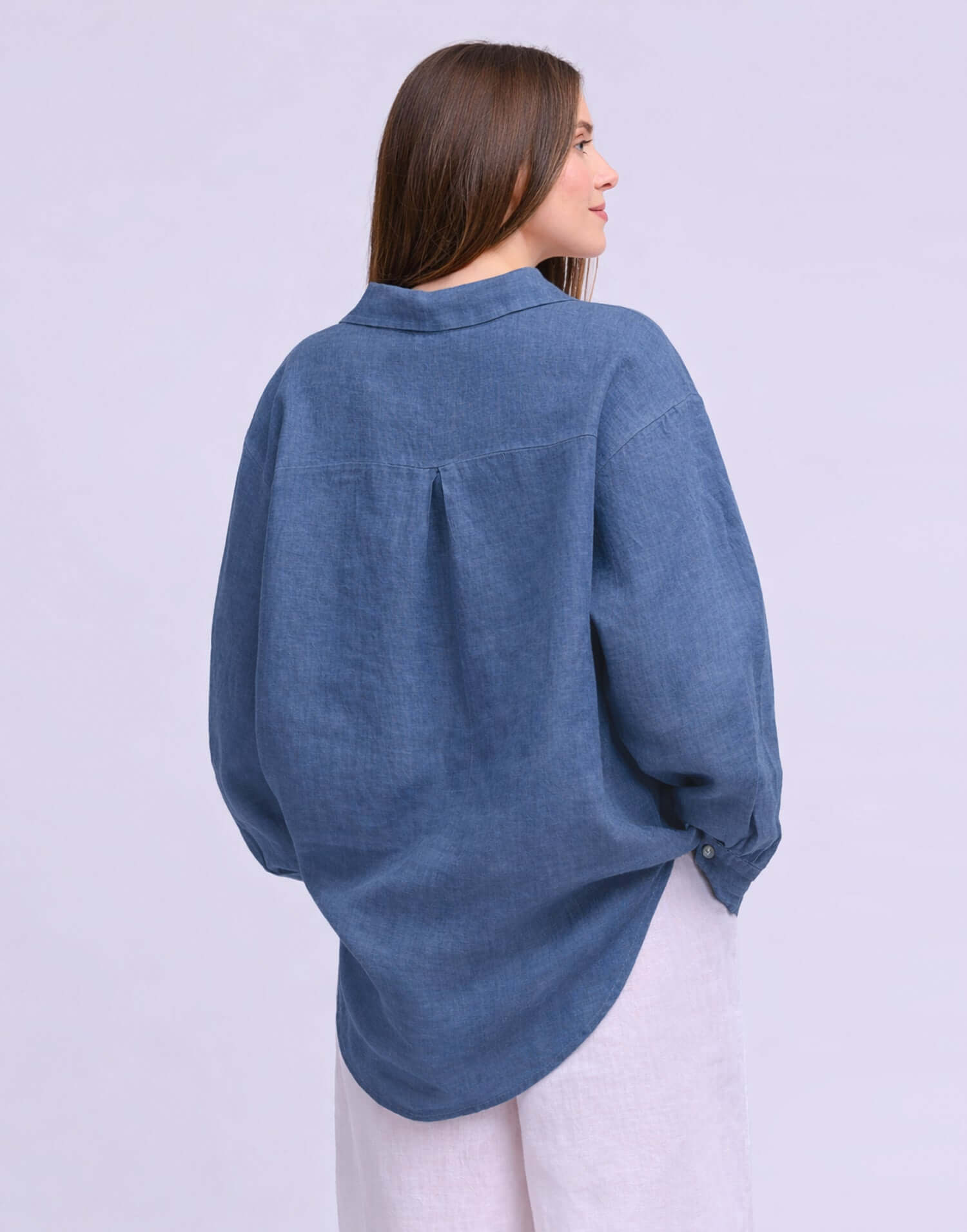 Back view of a model wearing the Yoga Jeans Elena Linen Oversized Button Up Top in denim blue.
